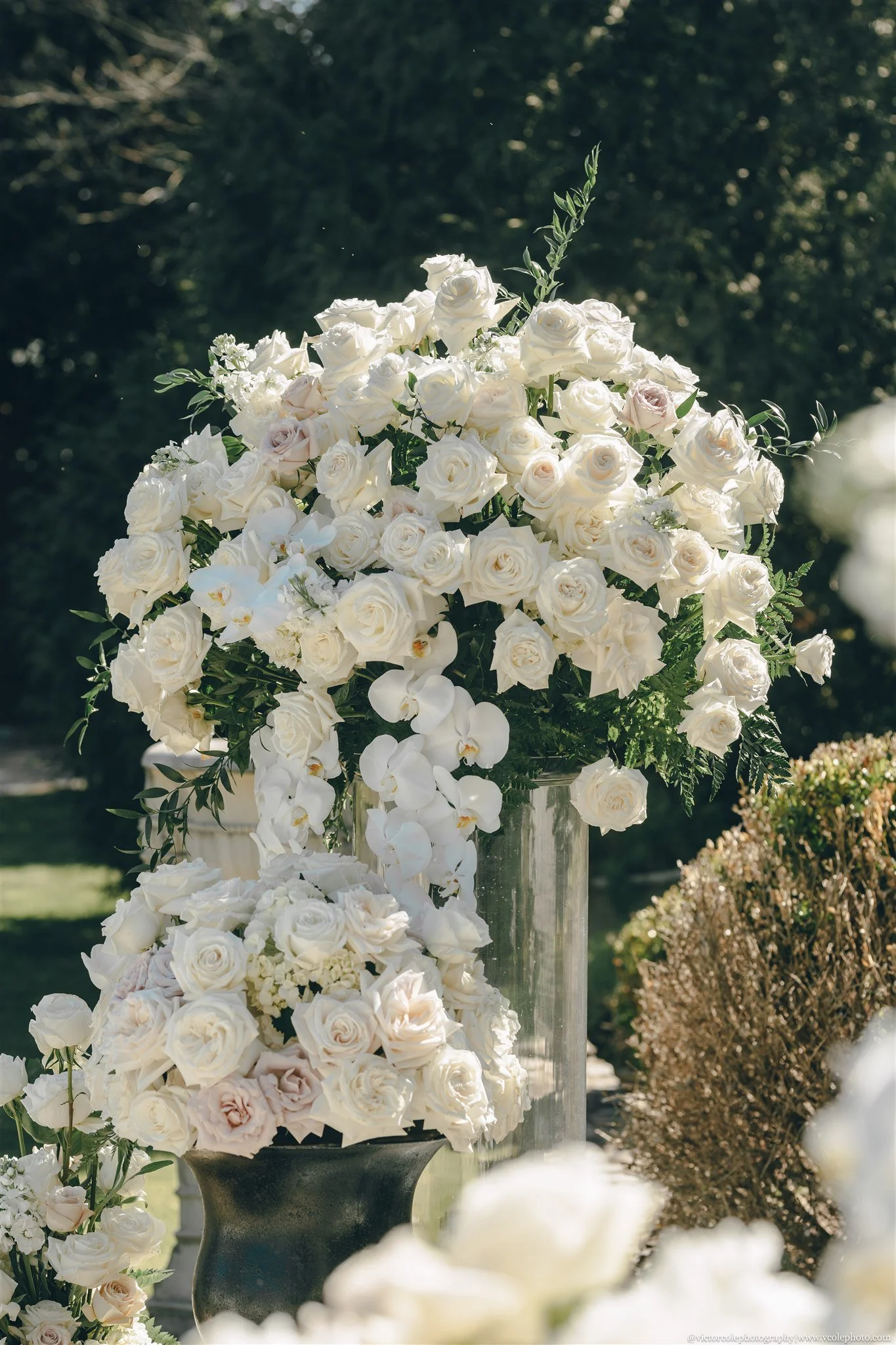 Large bouquet of white roses and white orchids on a podium at an outdoor event.