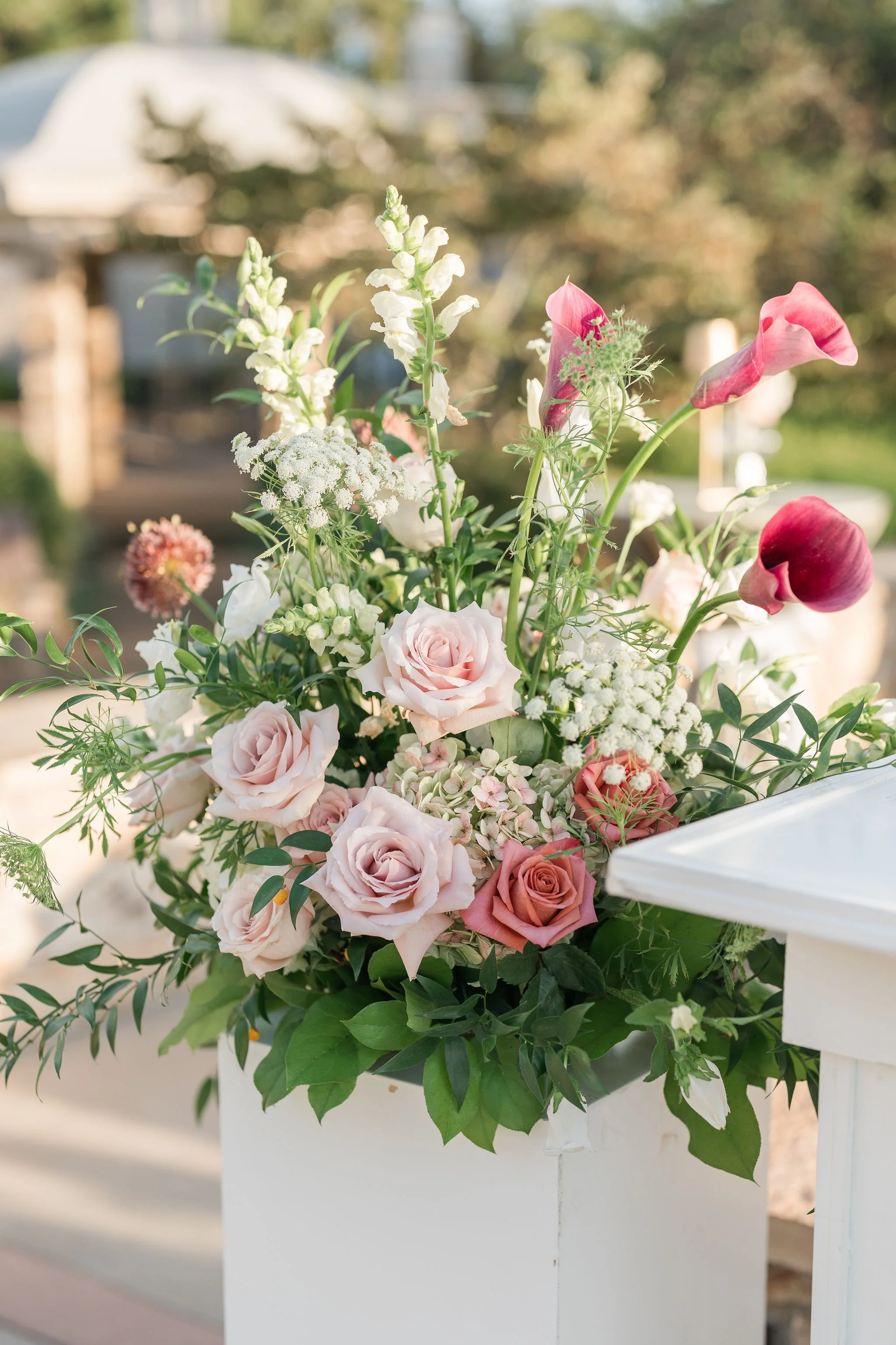 Bouquet of pink, white, and cream roses, calla lilies, and other flowers in a white container.