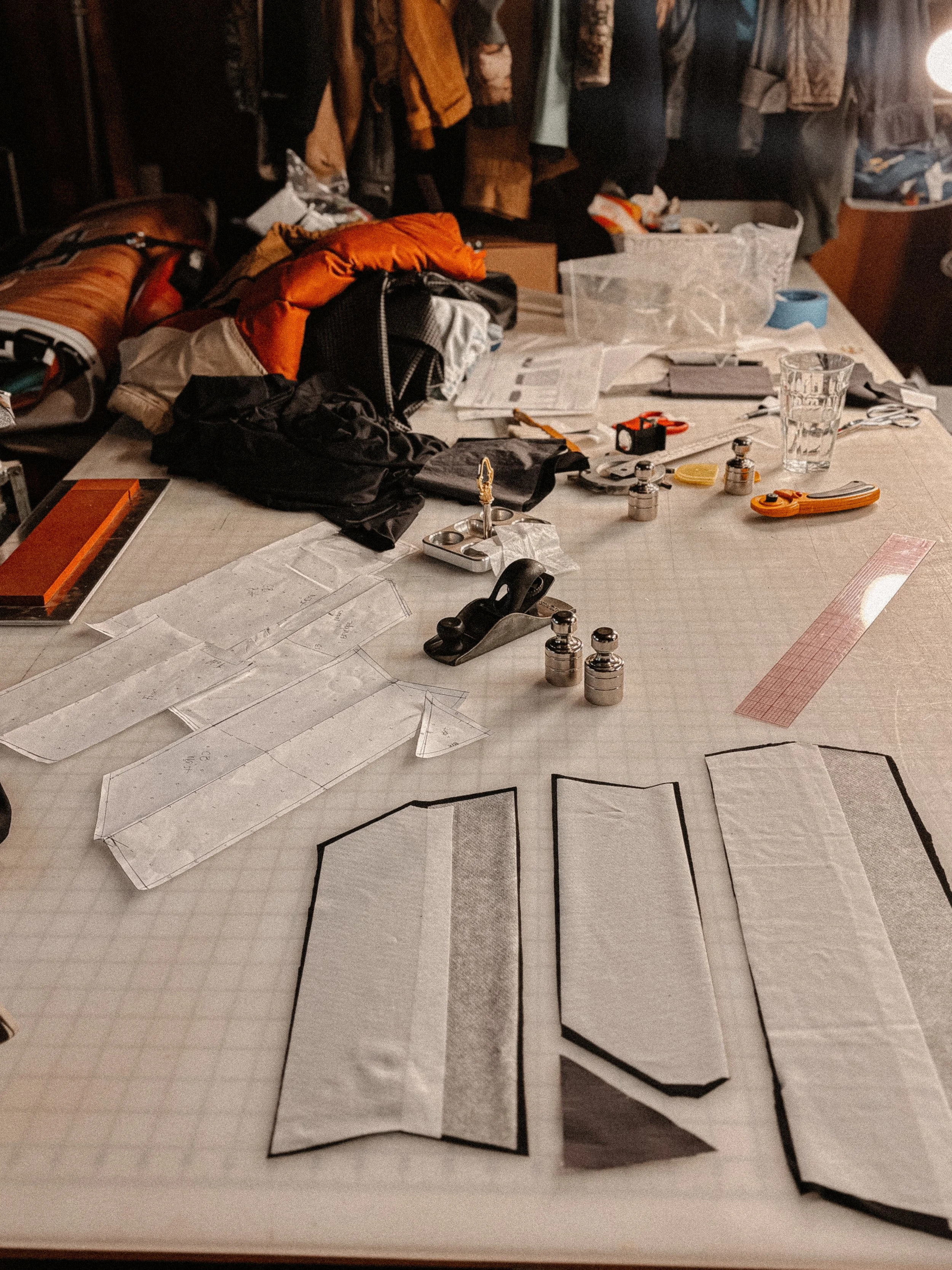 Outdoor apparel designer's worktable covered with fabric, clothing patterns, sewing tools, and garments, during mock-up building and prototyping process.