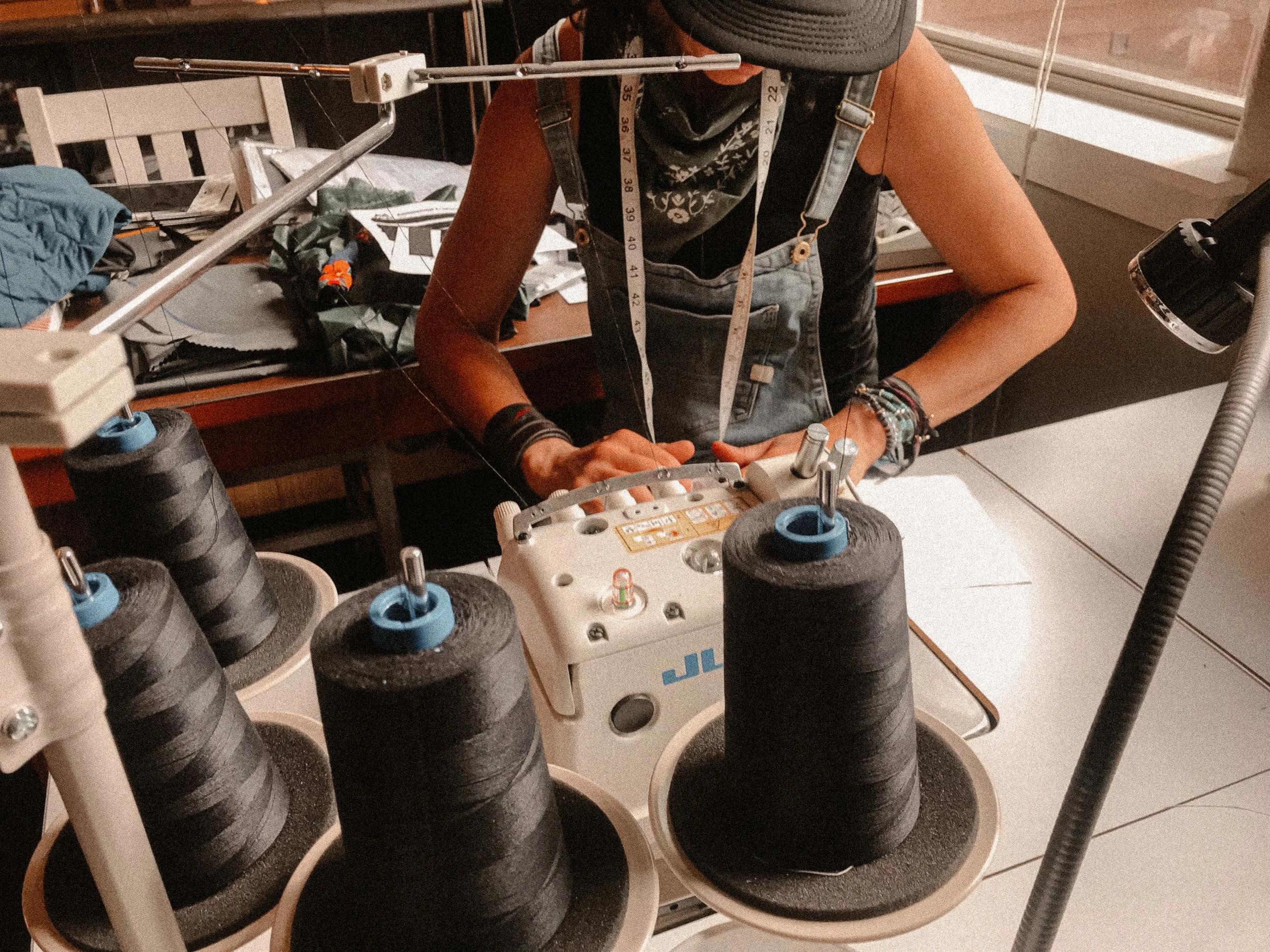 Textile artist operating a vintage industrial loom surrounded by oversized black yarn spools