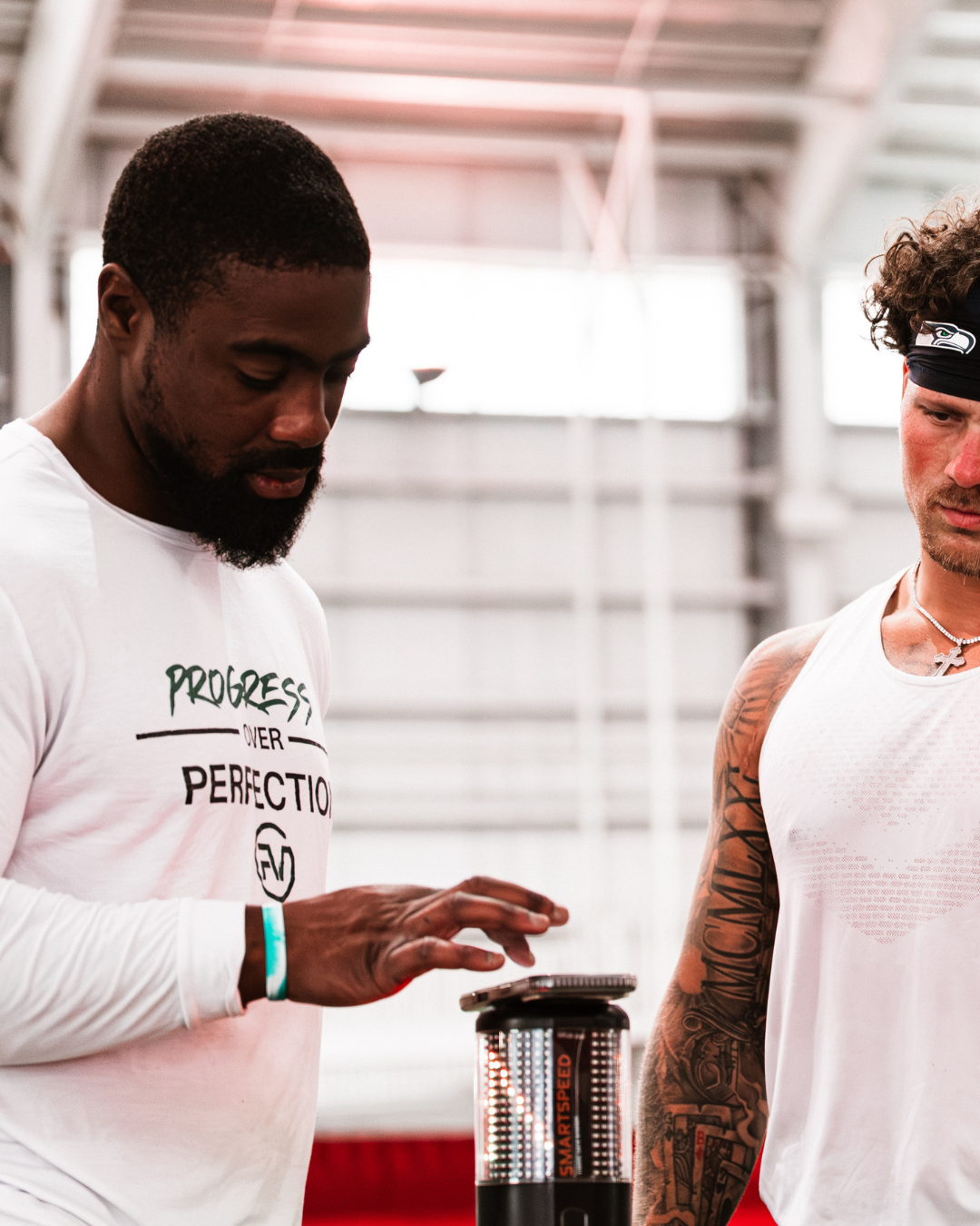 An athlete with a coach with athletic builds standing in an college facility, looking at their training data from the athlete's sprinting.