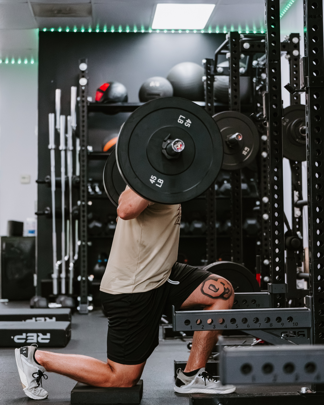 Athlete lifting a barbell with weights in a gym with black racks and workout equipment.
