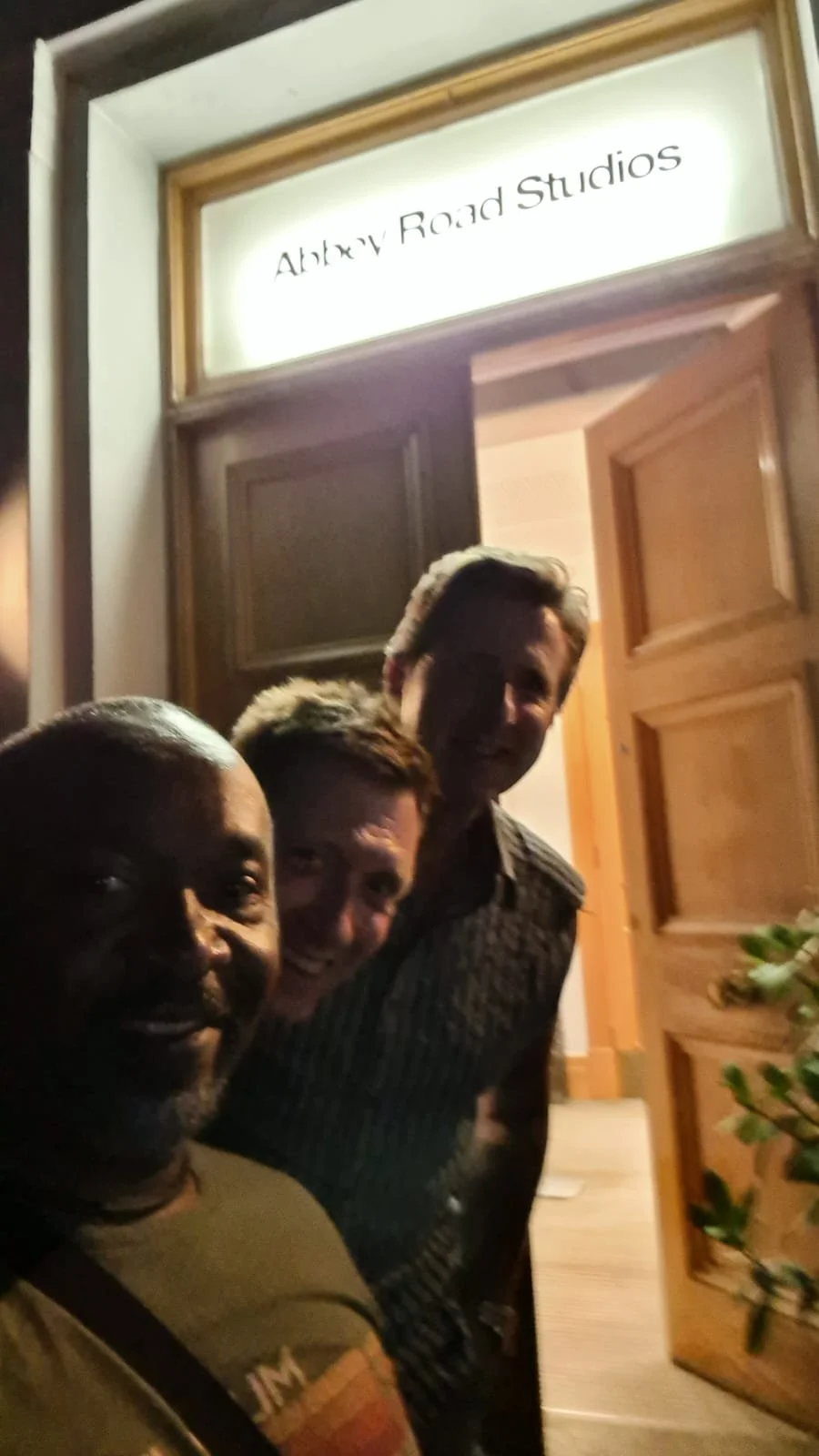 Three people smiling and taking a selfie in front of a door with a sign that reads 'Alkry Road Studios'.