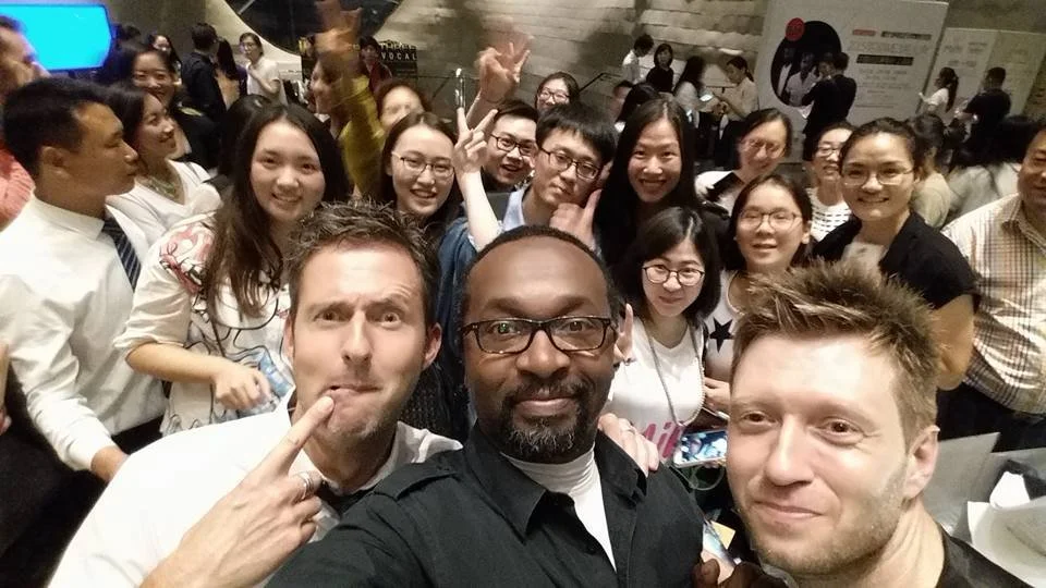 Group of people taking a selfie together at an indoor event or gathering, with many smiling and posing for the camera.