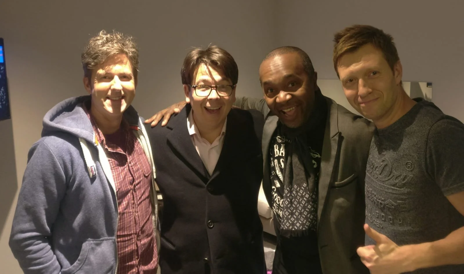 Four men standing close together and smiling for a photo indoors.