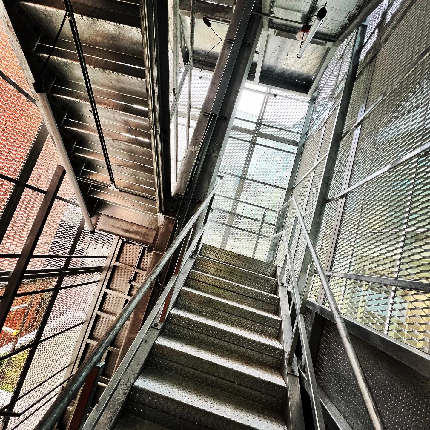 View up the steel fire escape flights, with handrails and architectural mesh enclosure.