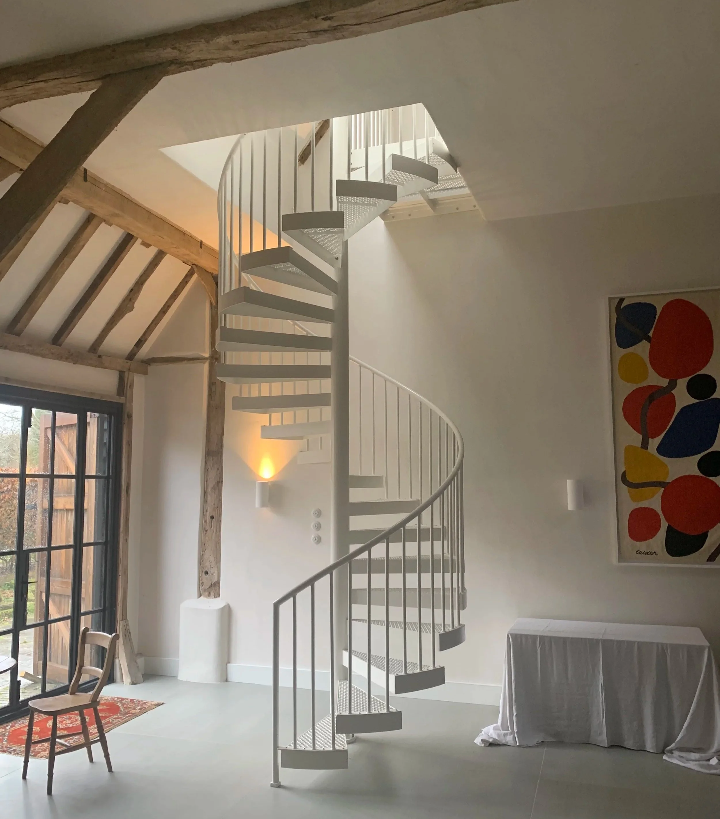 White steel spiral staircase providing mezzanine access beneath exposed timber beams in Chailey.