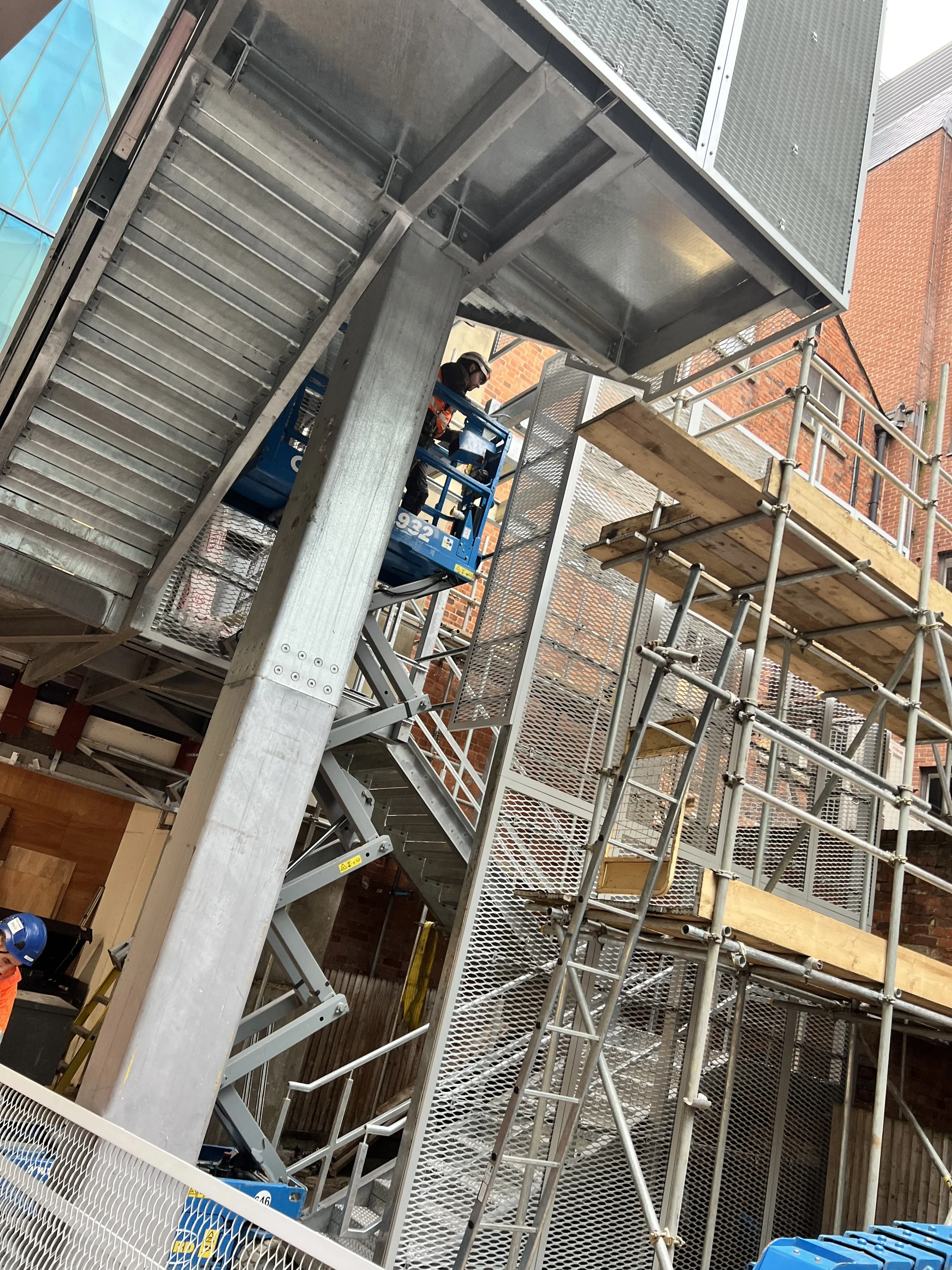 Galvanised steel staircase and central supporting column during installation within surrounding scaffolding.