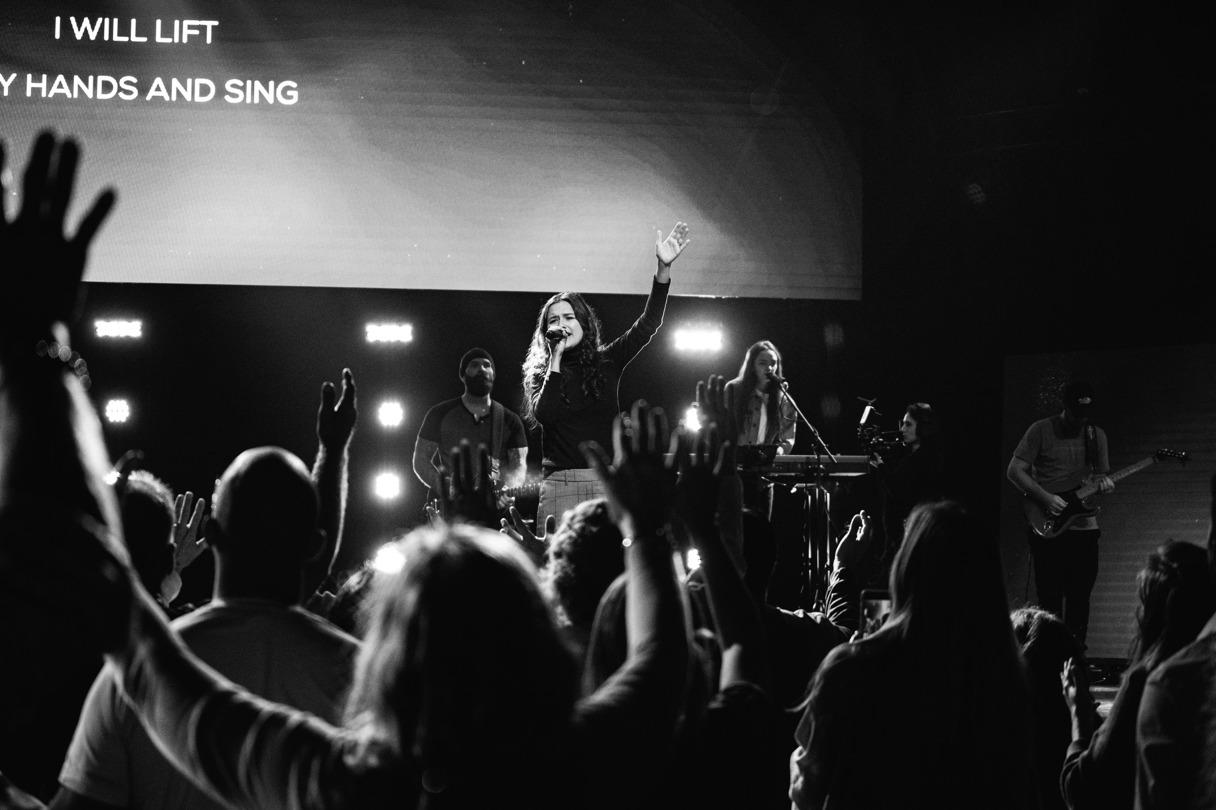 Worship leader singing on stage as the crowd raises their hands, black and white