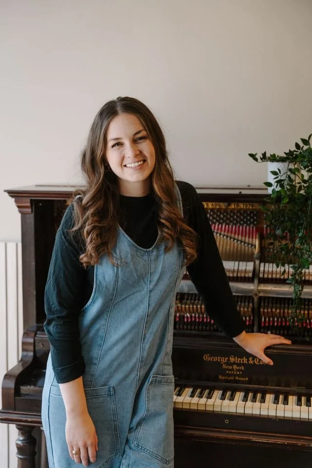 Caroline Bosley, founder and head coach of The Vocal Society, smiling beside a piano