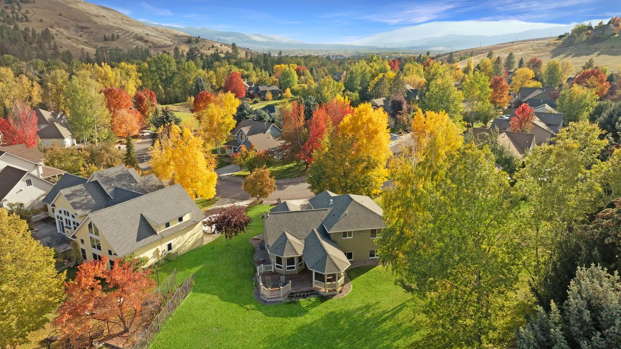 Aerial view of a Missoula, Montana neighborhood with homes, colorful fall trees, and surrounding mountains.