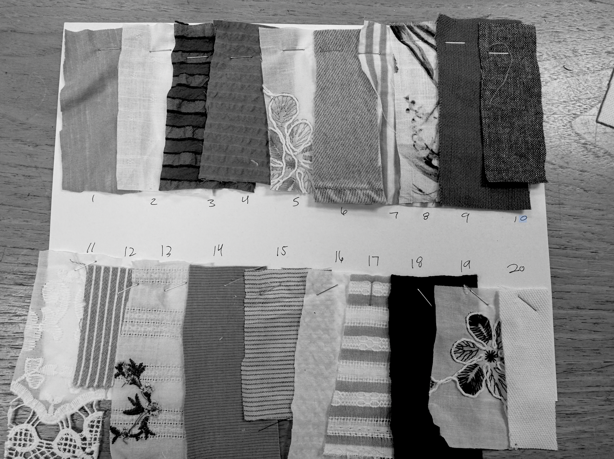A selection of fabric swatches in different textures, patterns, and colors, pinned onto a white sheet with numbered labels, placed on a wooden surface.
