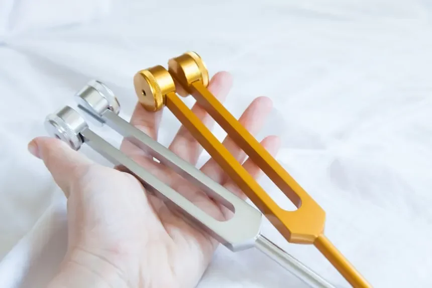 A hand holding two slingshots, one silver and one gold, against a light background.