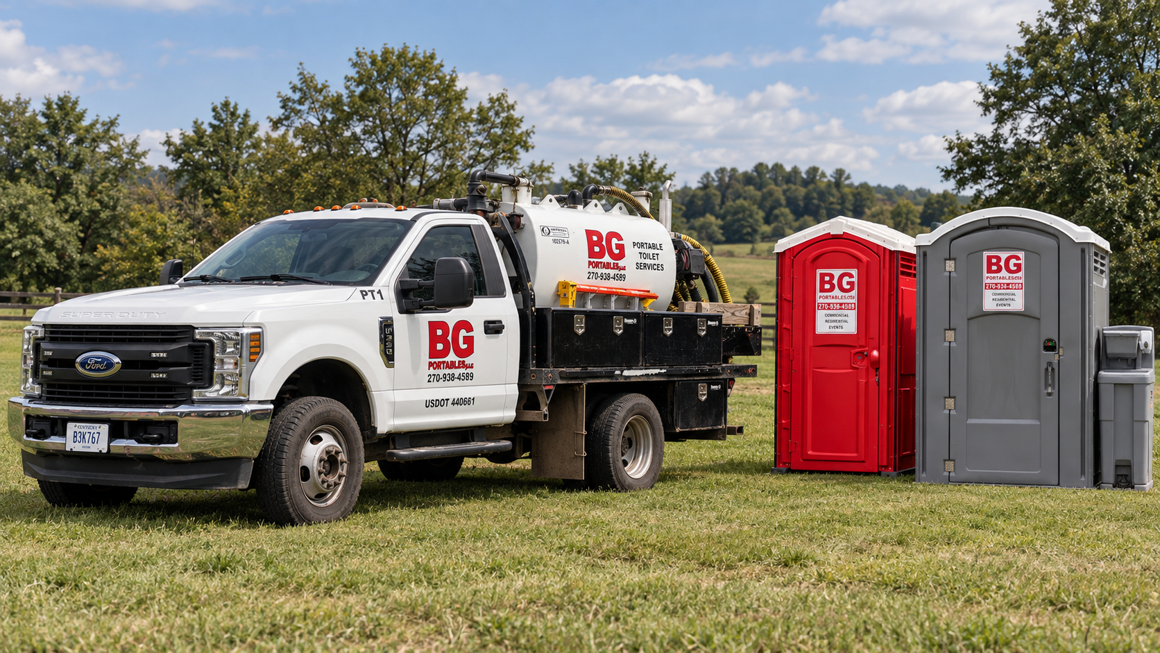 A white service truck with portable toilet rental company logos parked on grass, with a red and a gray portable toilet beside it, set outdoors under a cloudy sky.