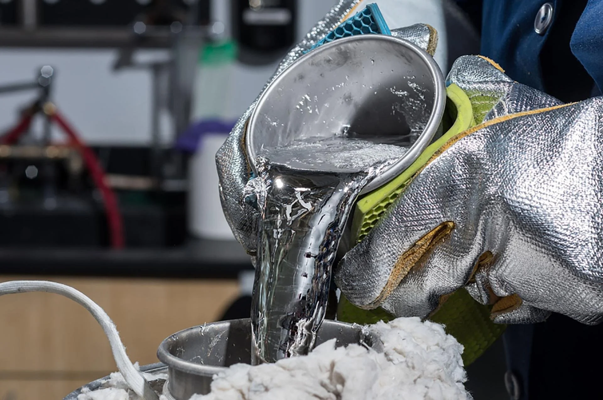 A person wearing a silver heat-resistant glove pouring a metallic liquid