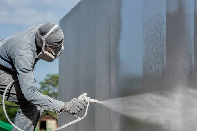 A person wearing protective gear spraycoating an external facade