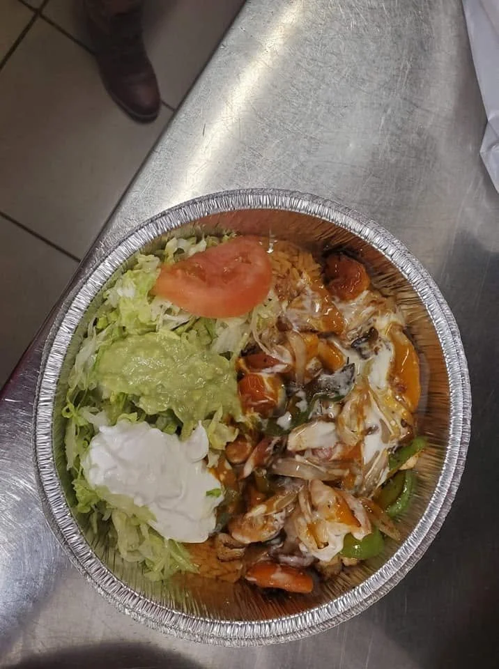 Foil container with lettuce, tomato, guacamole, sour cream, shredded chicken with vegetables and sauce.