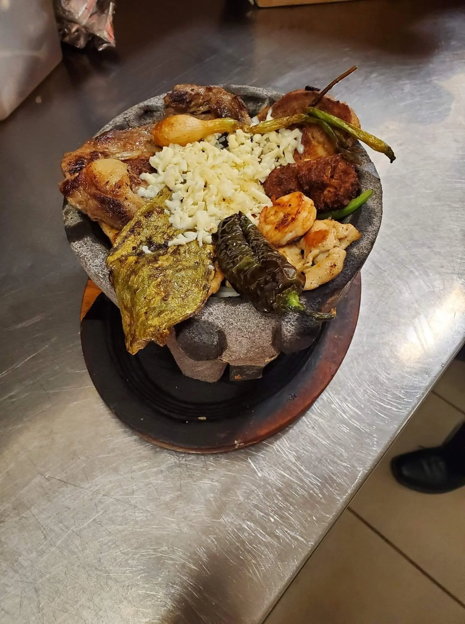 A traditional Mexican molcajete filled with cooked meat, grilled vegetables, cheese, and shrimp, resting on a table.