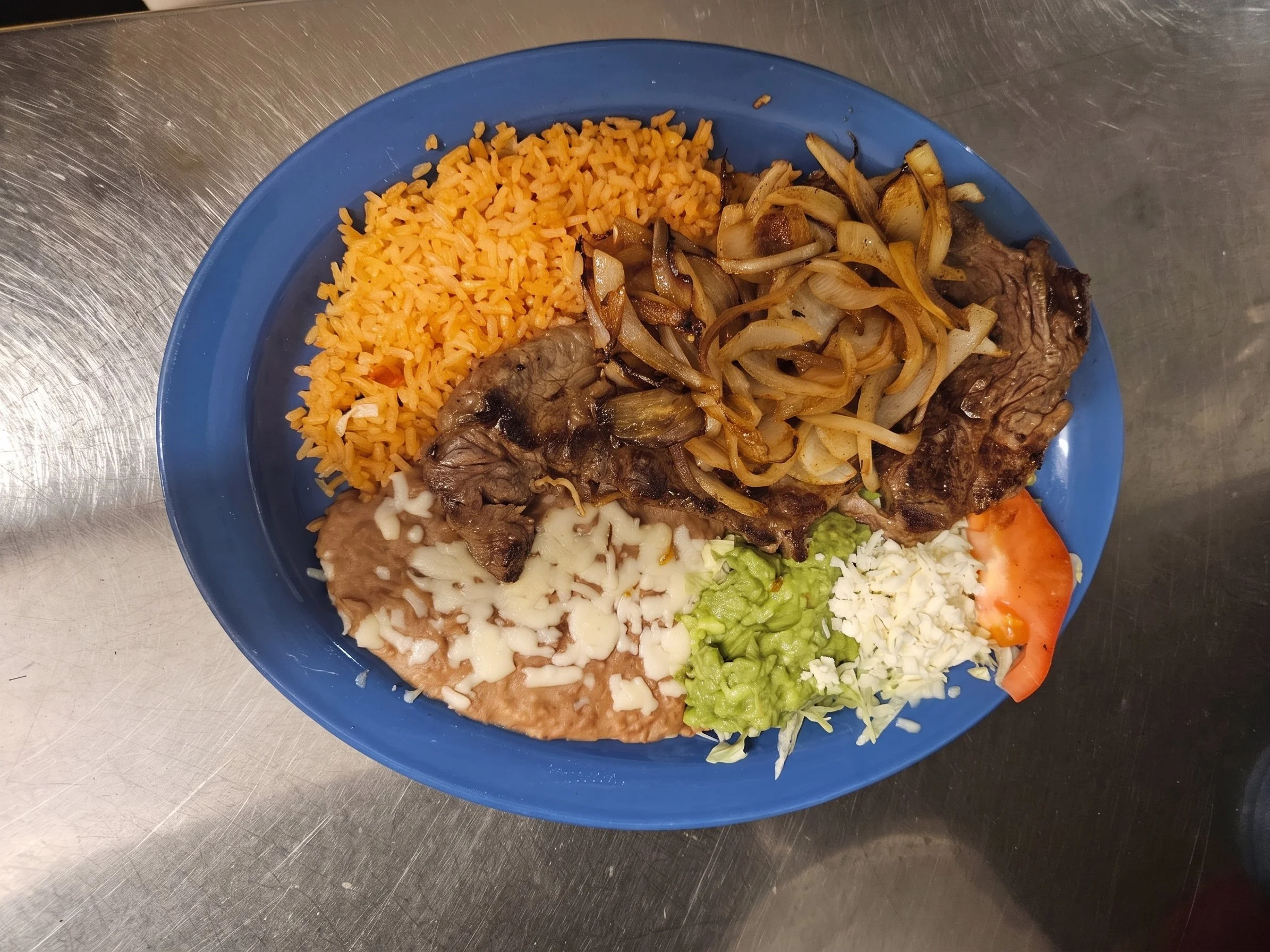 A colorful plate of Mexican food with rice, roasted vegetables, refried beans topped with cheese, lettuce, tomato, and grilled meat.