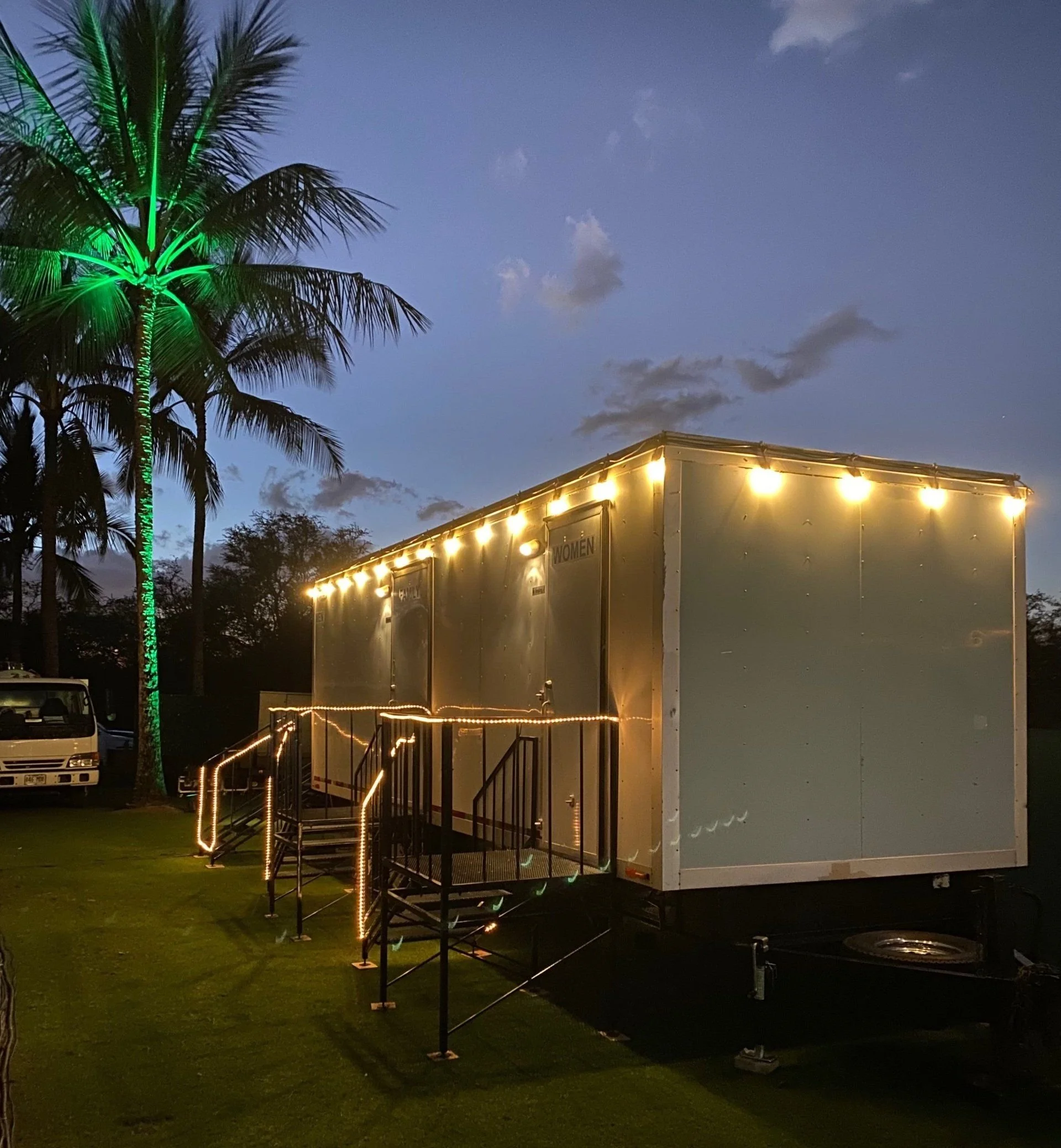 Side view of an illuminated event restroom trailer at night.