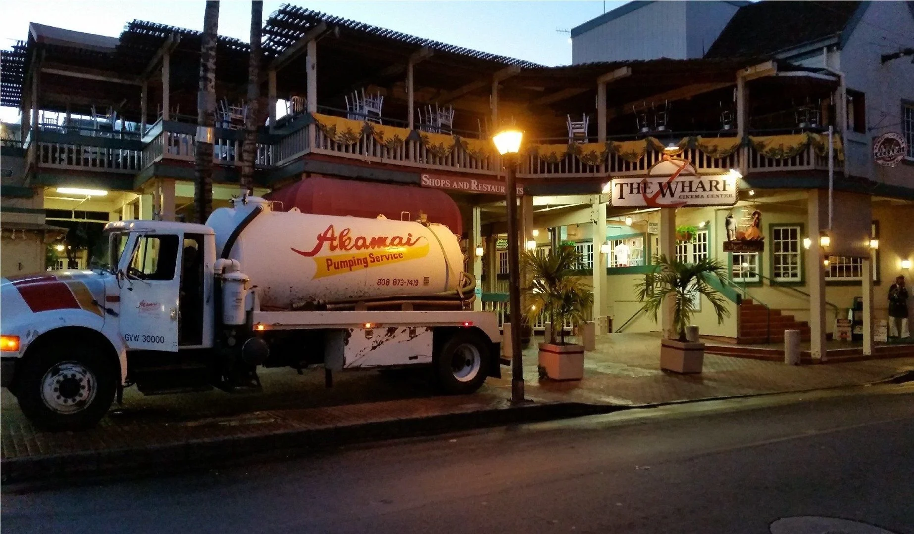Akamai Pumping Service truck outside a Maui waterfront restaurant at night.