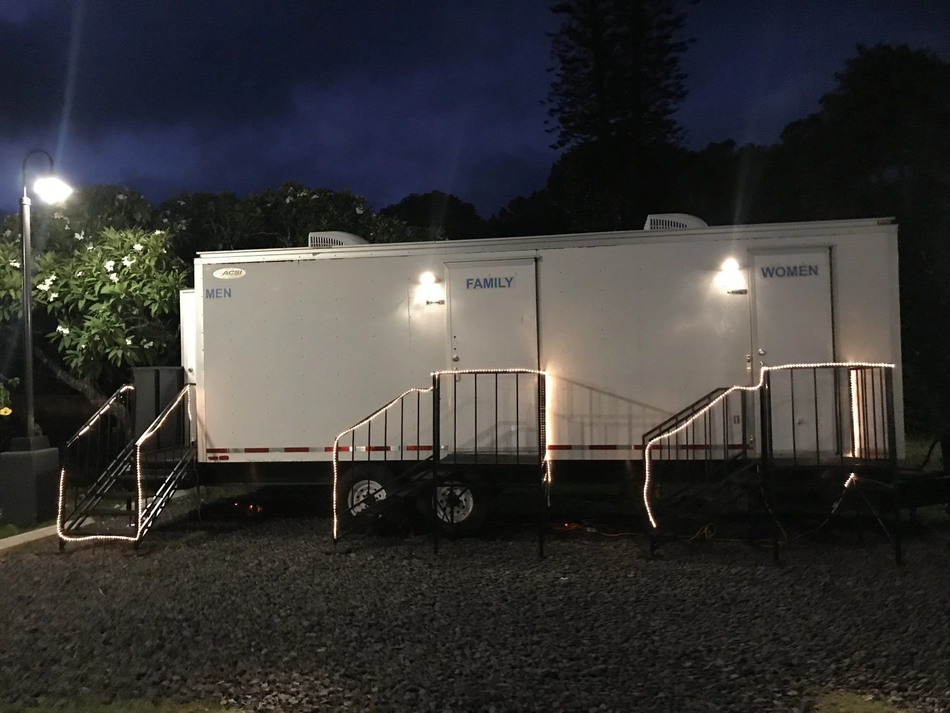 Event restroom trailer illuminated at night.