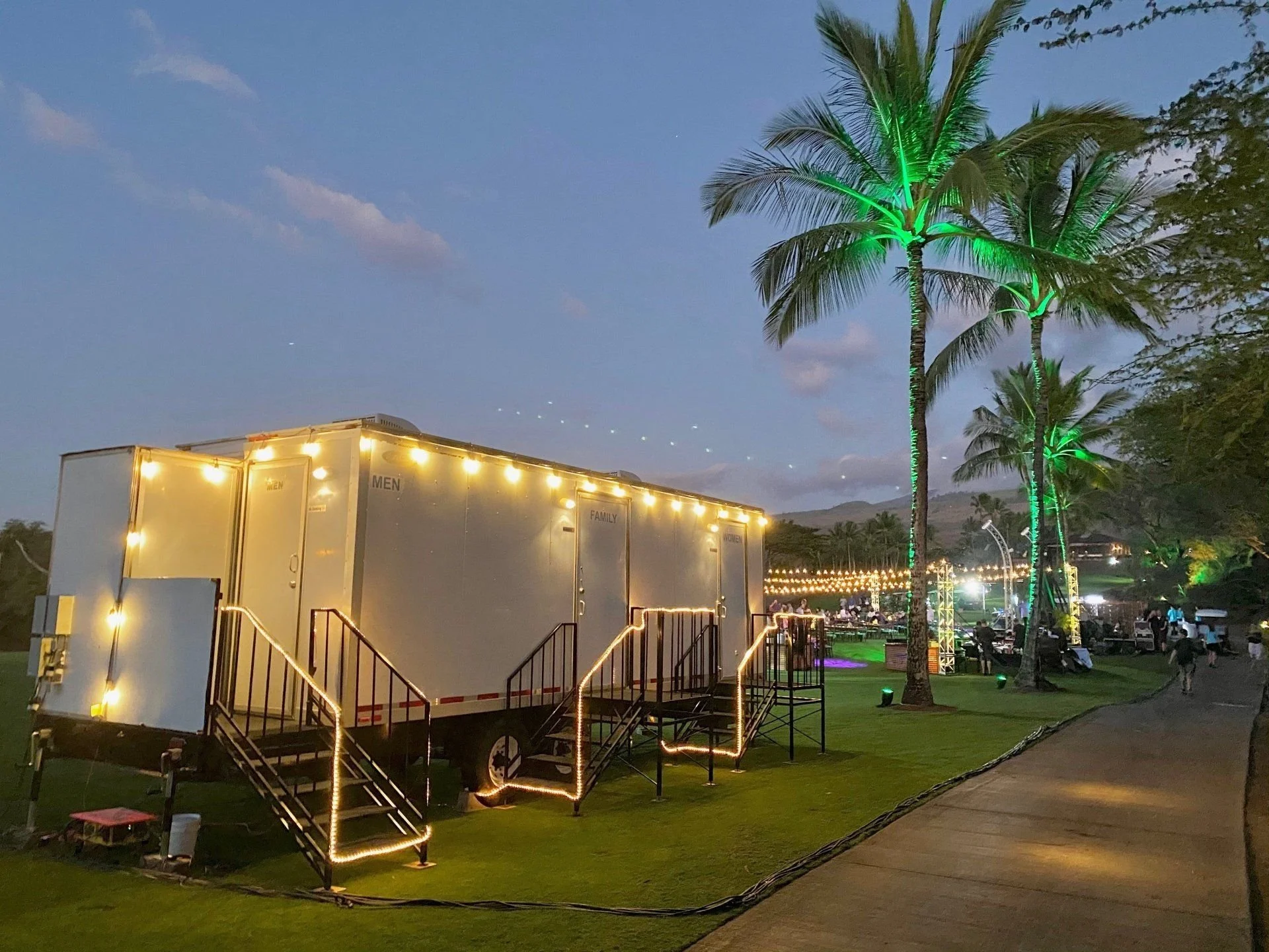 Illuminated restroom trailer at an evening event.
