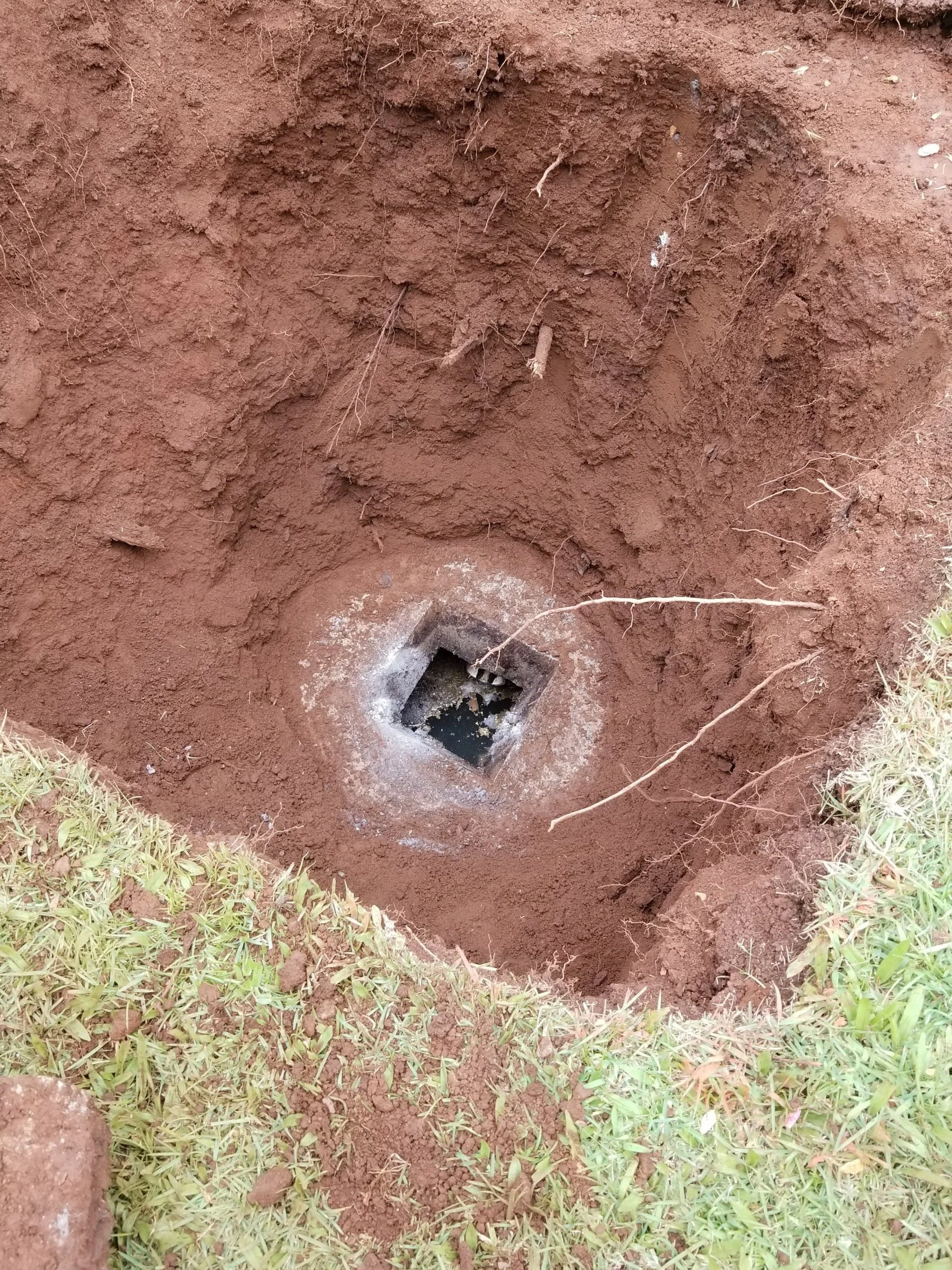 Concrete access opening exposed in red soil.