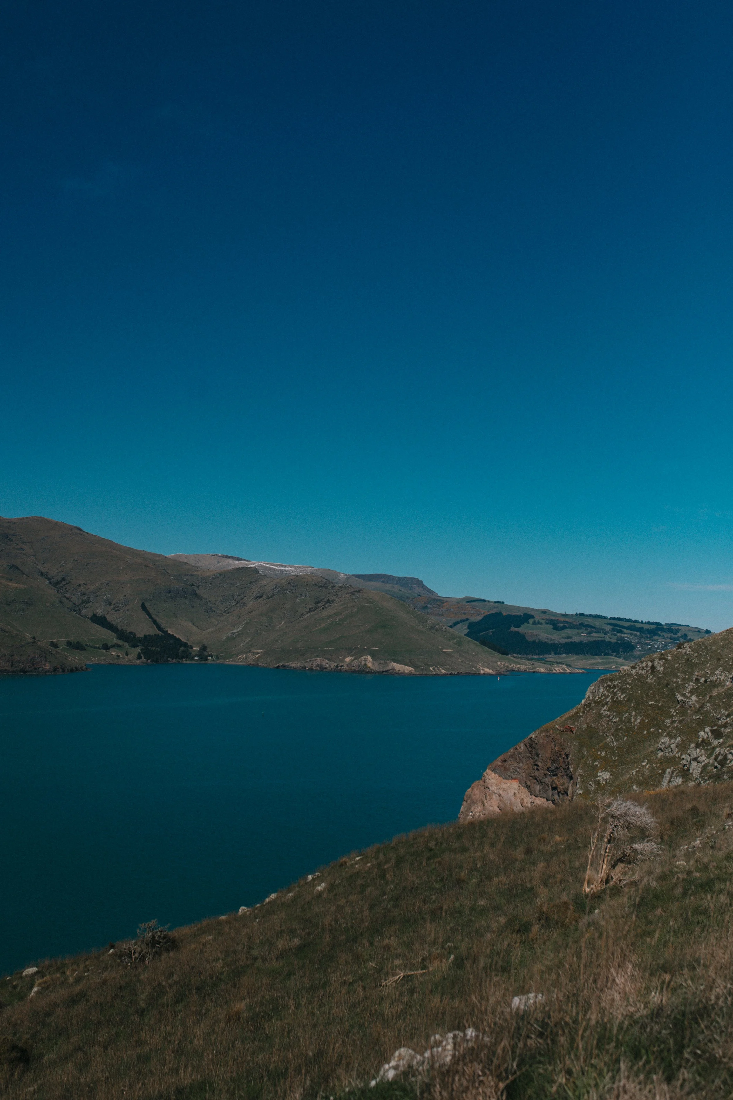 Scenic view of a large lake surrounded by rolling hills with a clear blue sky above.