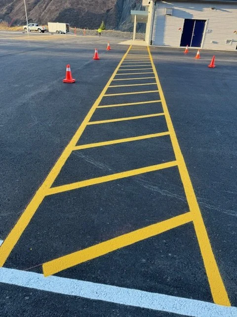 Newly painted yellow diagonal-striped parking space with orange cones around it in a parking lot.