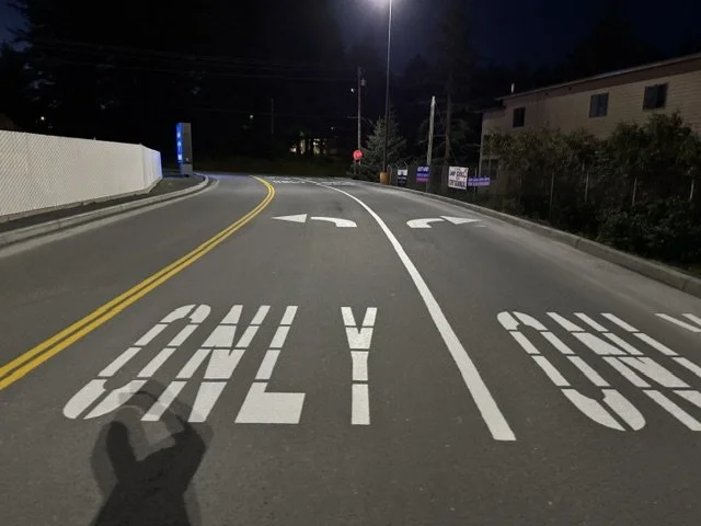 Empty street at night with road markings for "ONLY" and arrows indicating traffic directions.