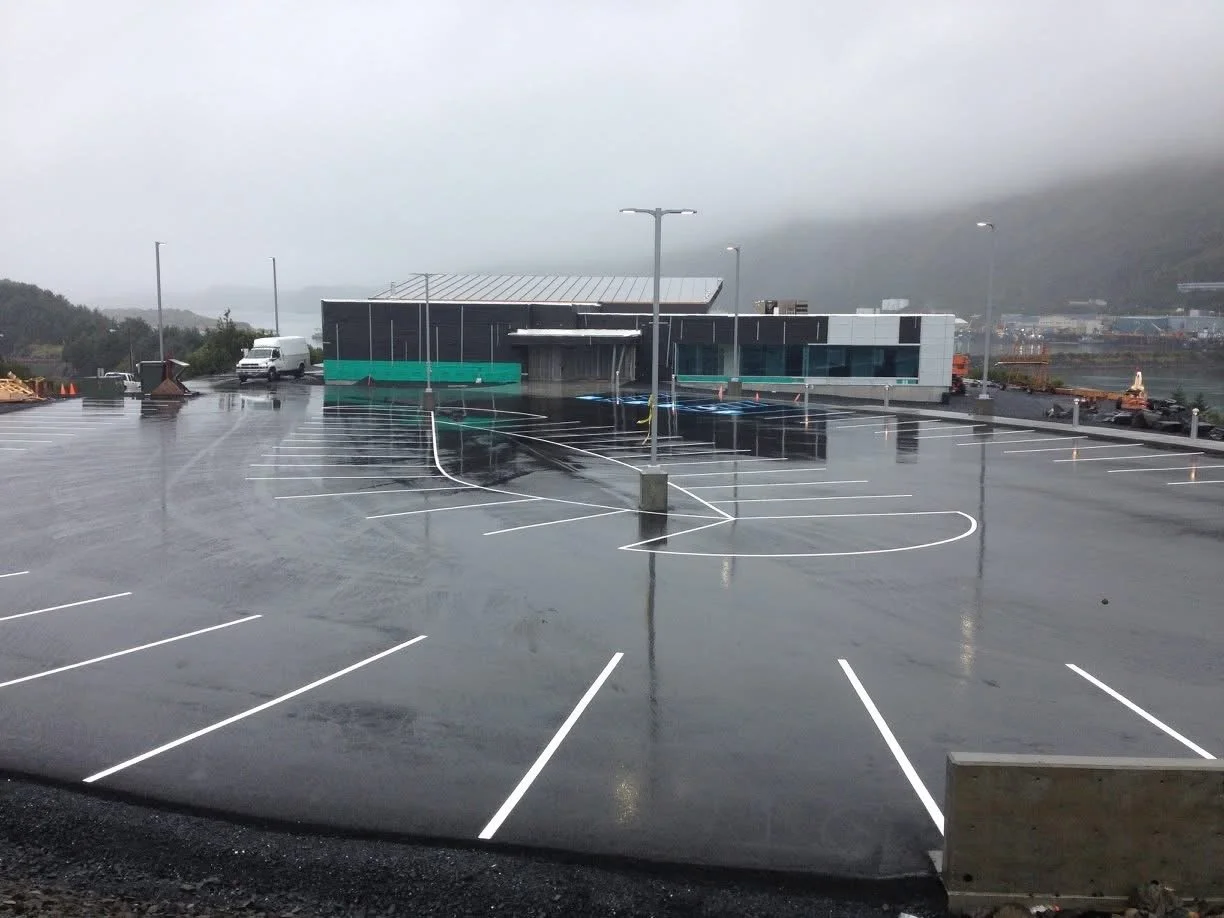 Empty parking lot with freshly painted spaces and a modern building in the background, on a rainy day with overcast sky.