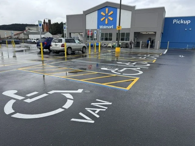 Walmart store entrance with a busy parking lot, handicap parking space, and a pickup area on a rainy day.