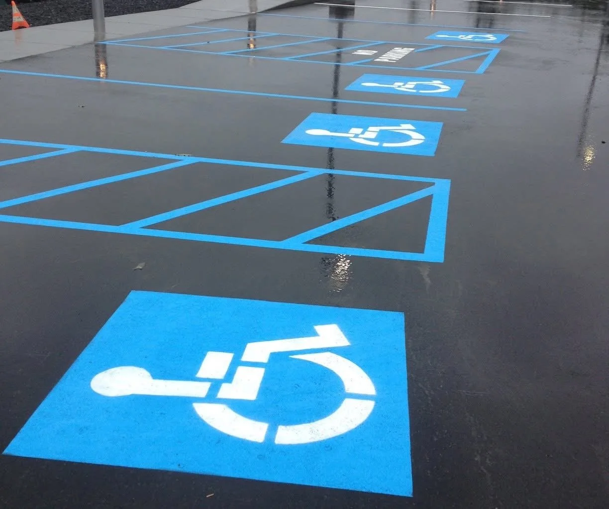 Parking lot with assigned accessible parking spaces marked by blue painted symbols and lines, including handicapped symbols.