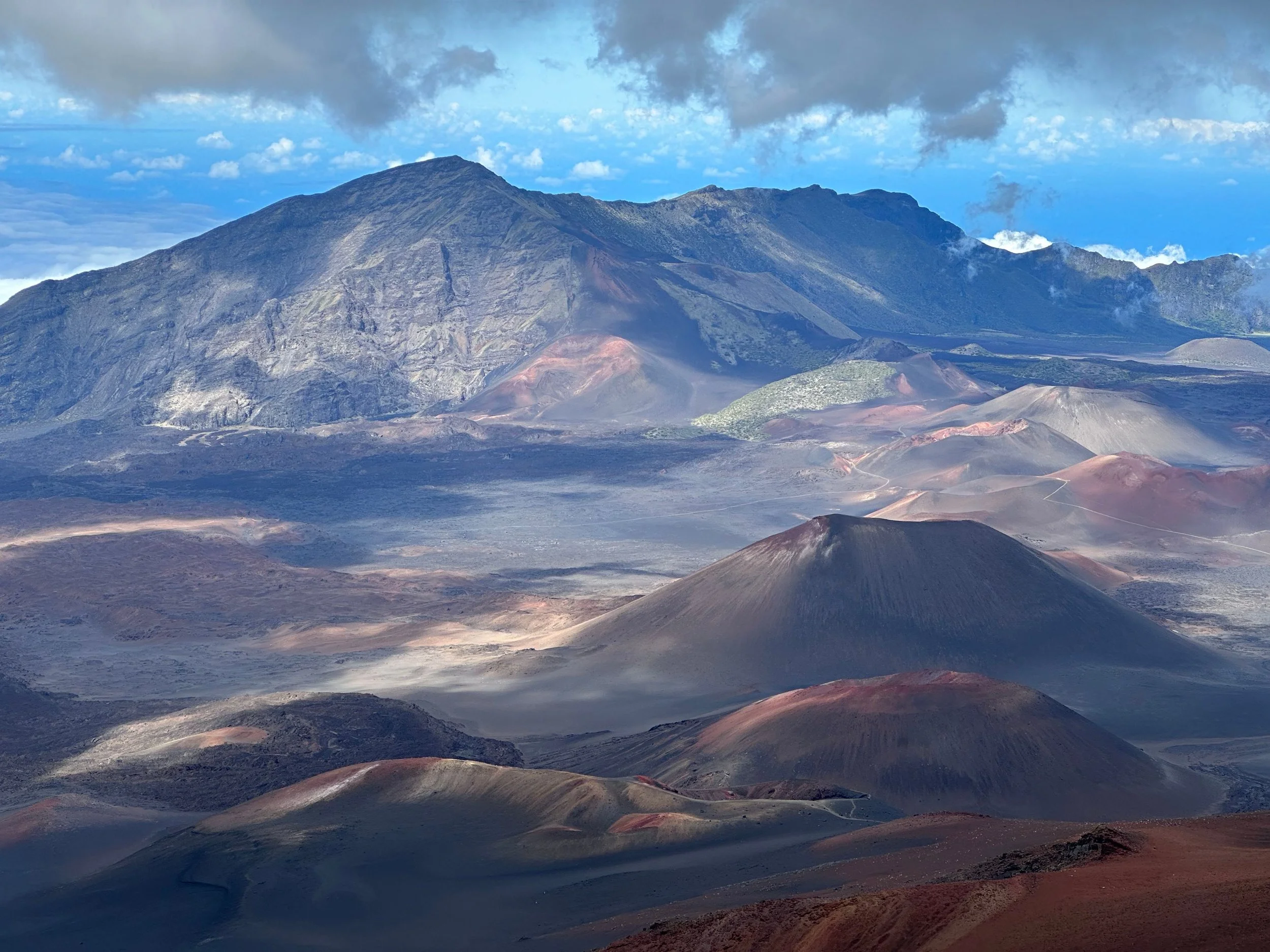 View of volcanic mountains with dark, rocky terrain and some smoke or steam rising, under a partly cloudy sky.