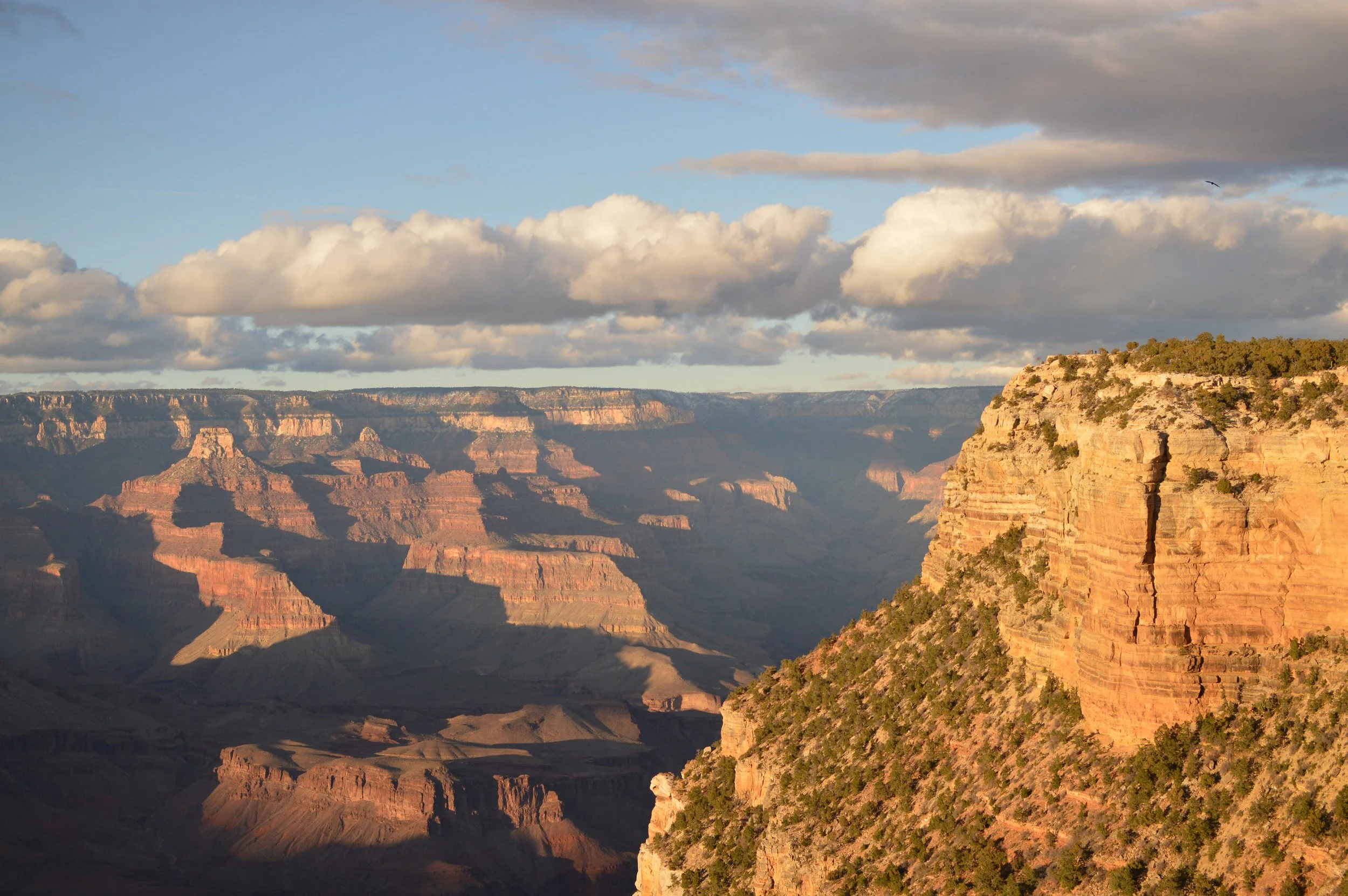 A scenic view of the Grand Canyon with layered rock formations and a partly cloudy sky.