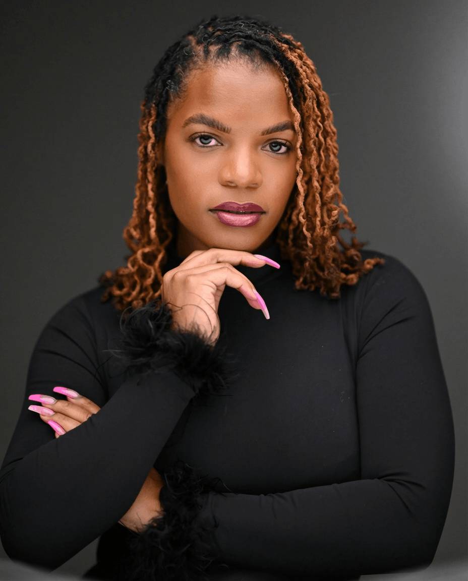 Portrait of a confident woman with curly two-tone hair, wearing a black top, against a dark background.