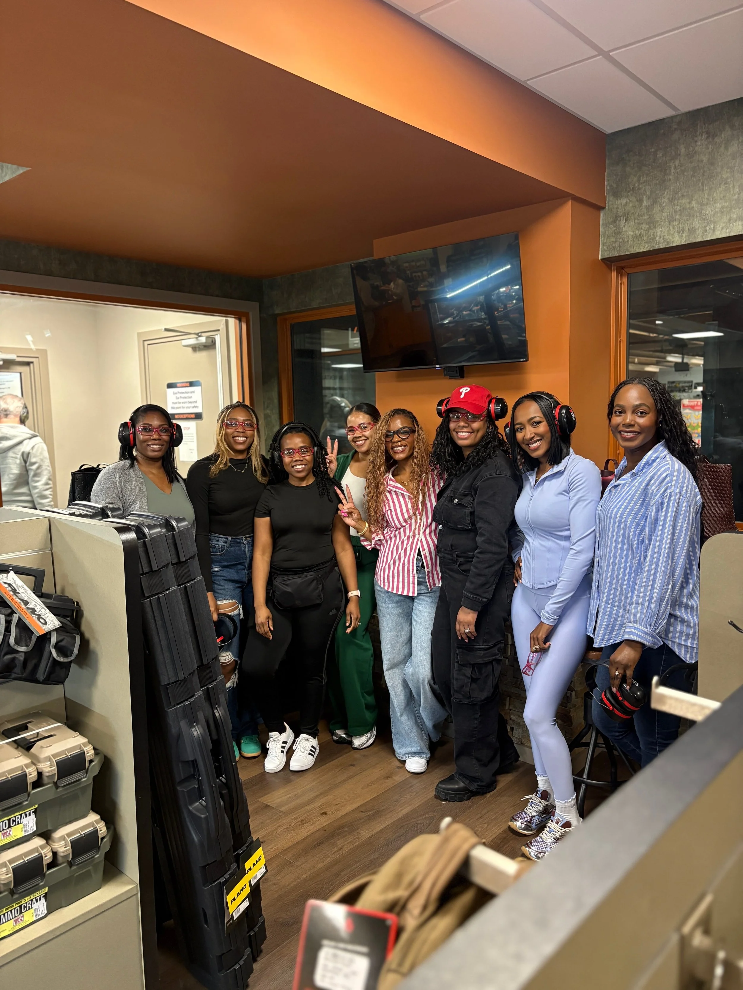 A group of seven women standing together indoors, smiling, some wearing headphones, in a retail store.