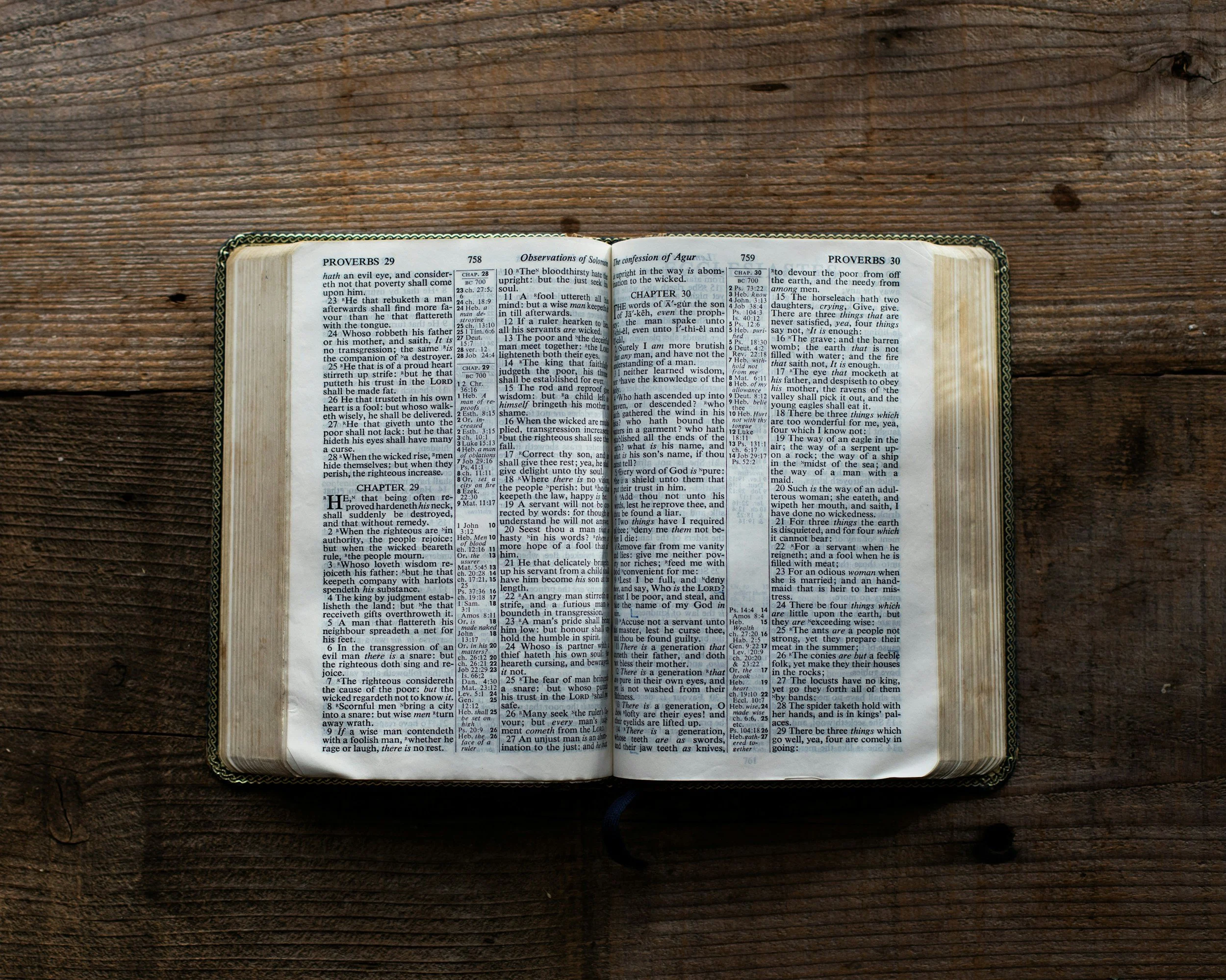 Open Bible on a wooden table, displaying verses from Proverbs and other chapters.