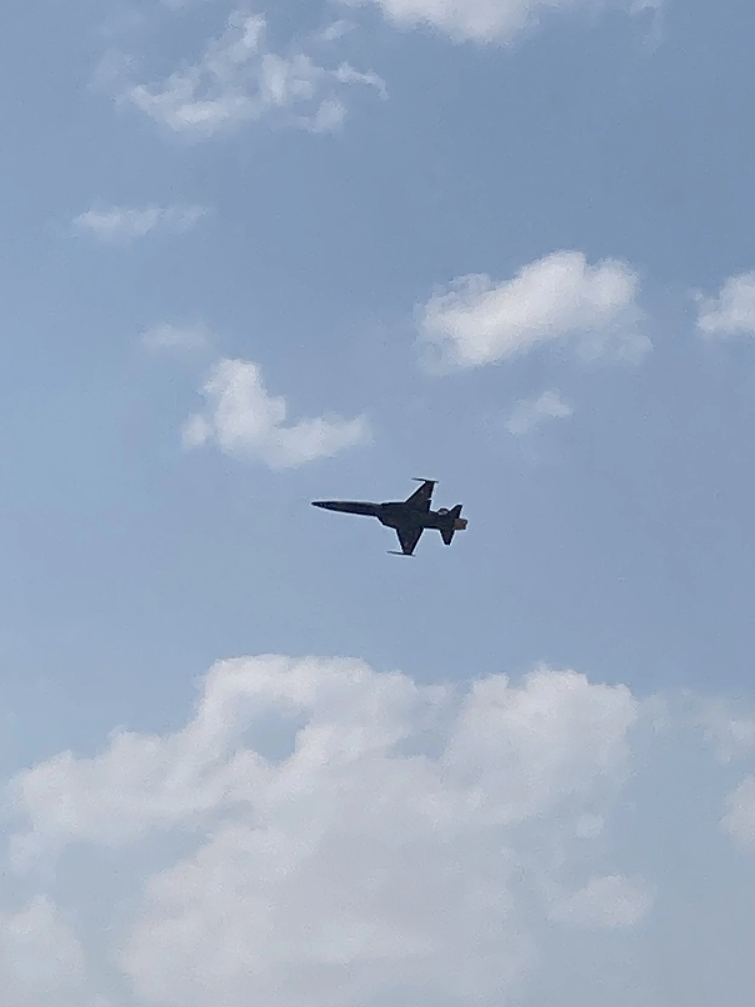 A military jet flying across a blue sky with white clouds.
