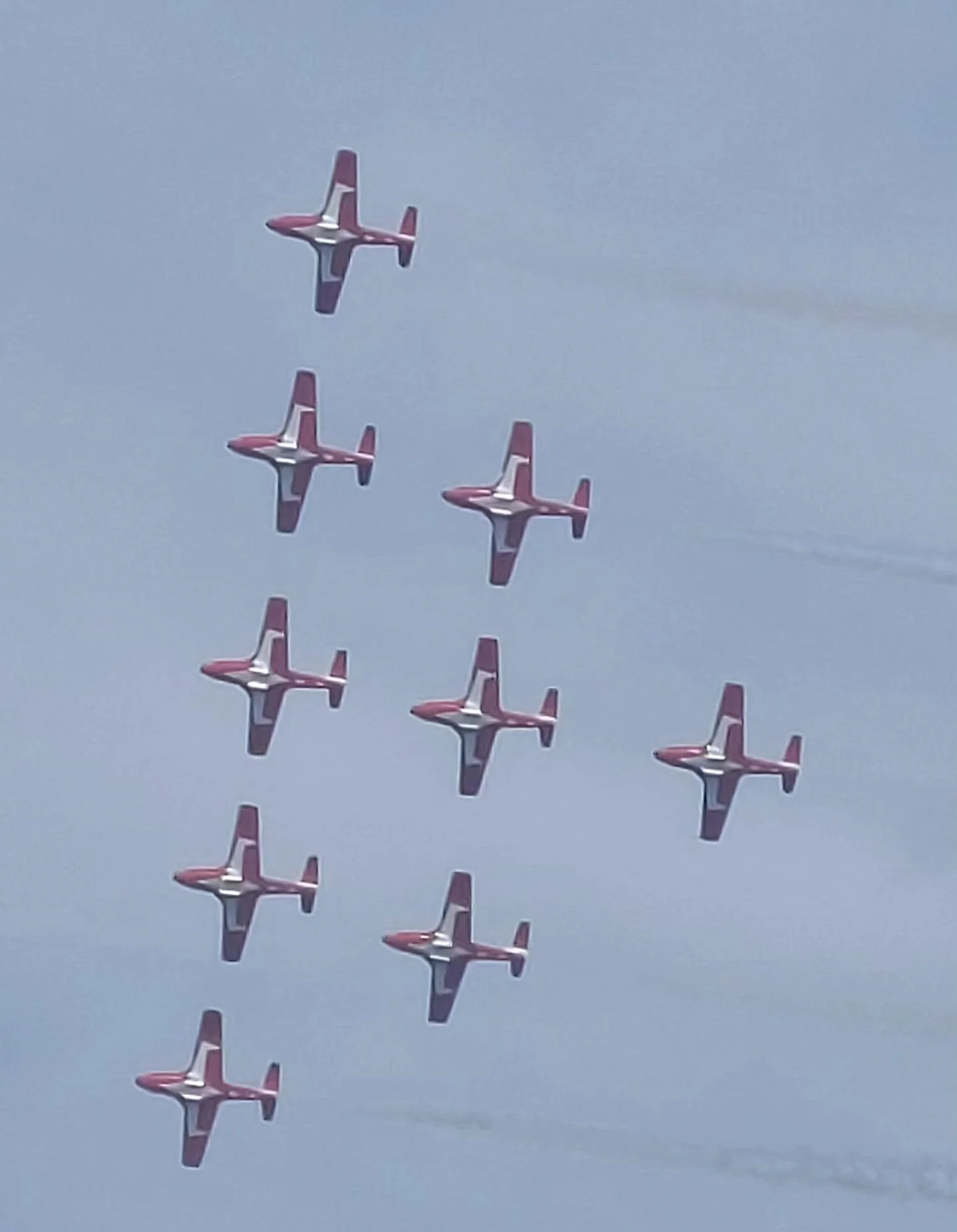 A formation of red, white, and blue fighter jets flying in a V-shape pattern through a cloudy sky.