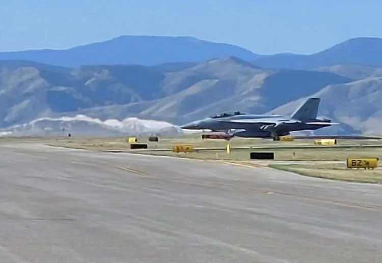 A fighter jet on a runway with mountains in the background.
