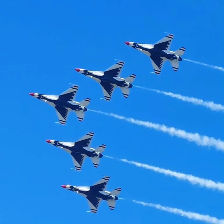 Five fighter jets flying in formation against a clear blue sky, leaving white smoke trails behind them.
