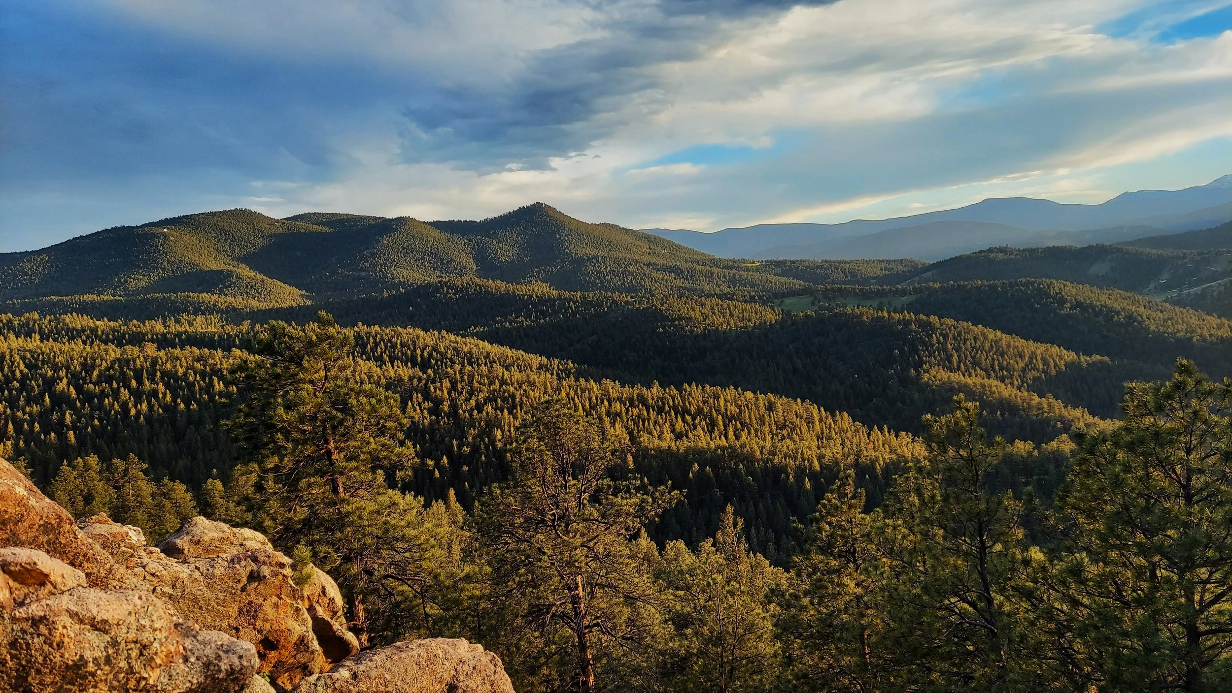 Scenic view of forested mountains under a partly cloudy sky with sunlight illuminating the trees.