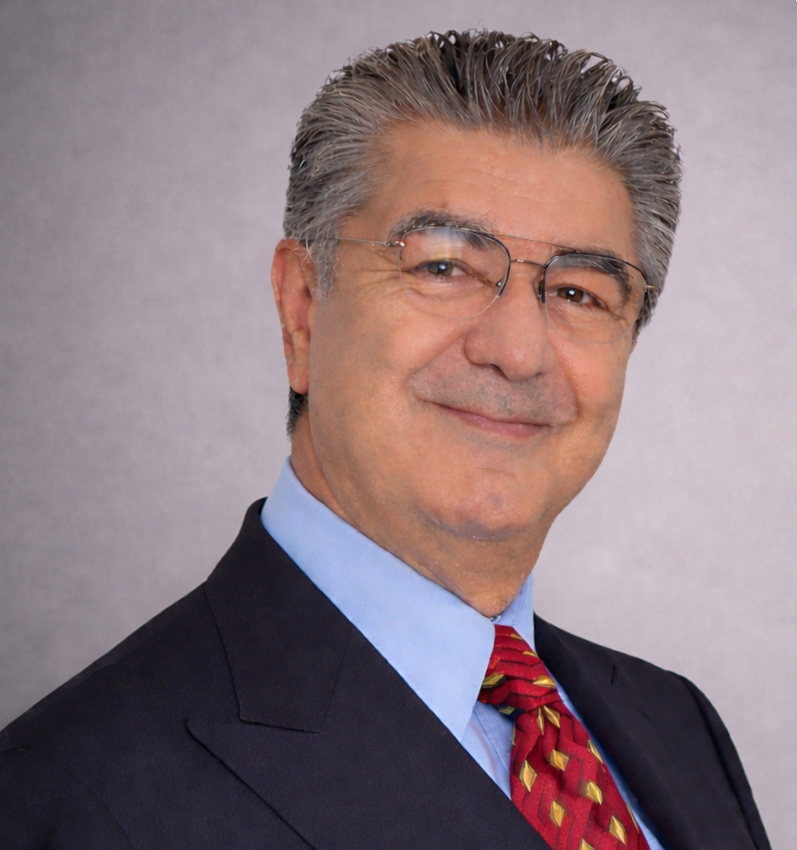 Portrait of a middle-aged man with gray hair, wearing glasses, a dark suit, blue shirt, and red tie, smiling at the camera against a plain background.