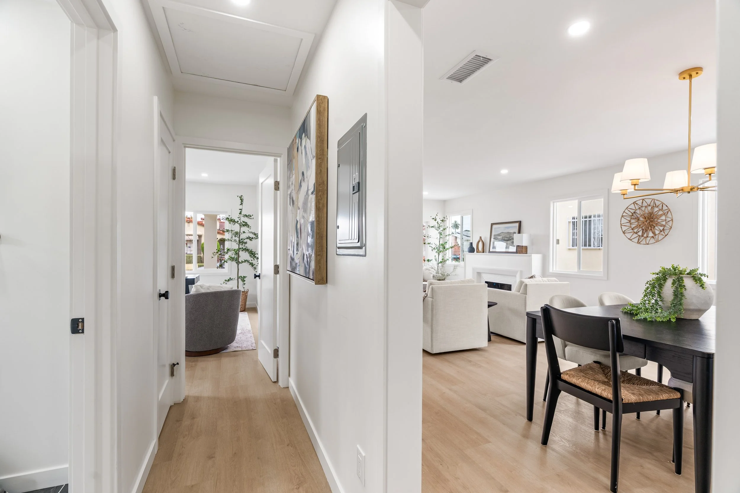 View of a modern living room and dining area with white walls, light wood flooring, windows, and contemporary decor.