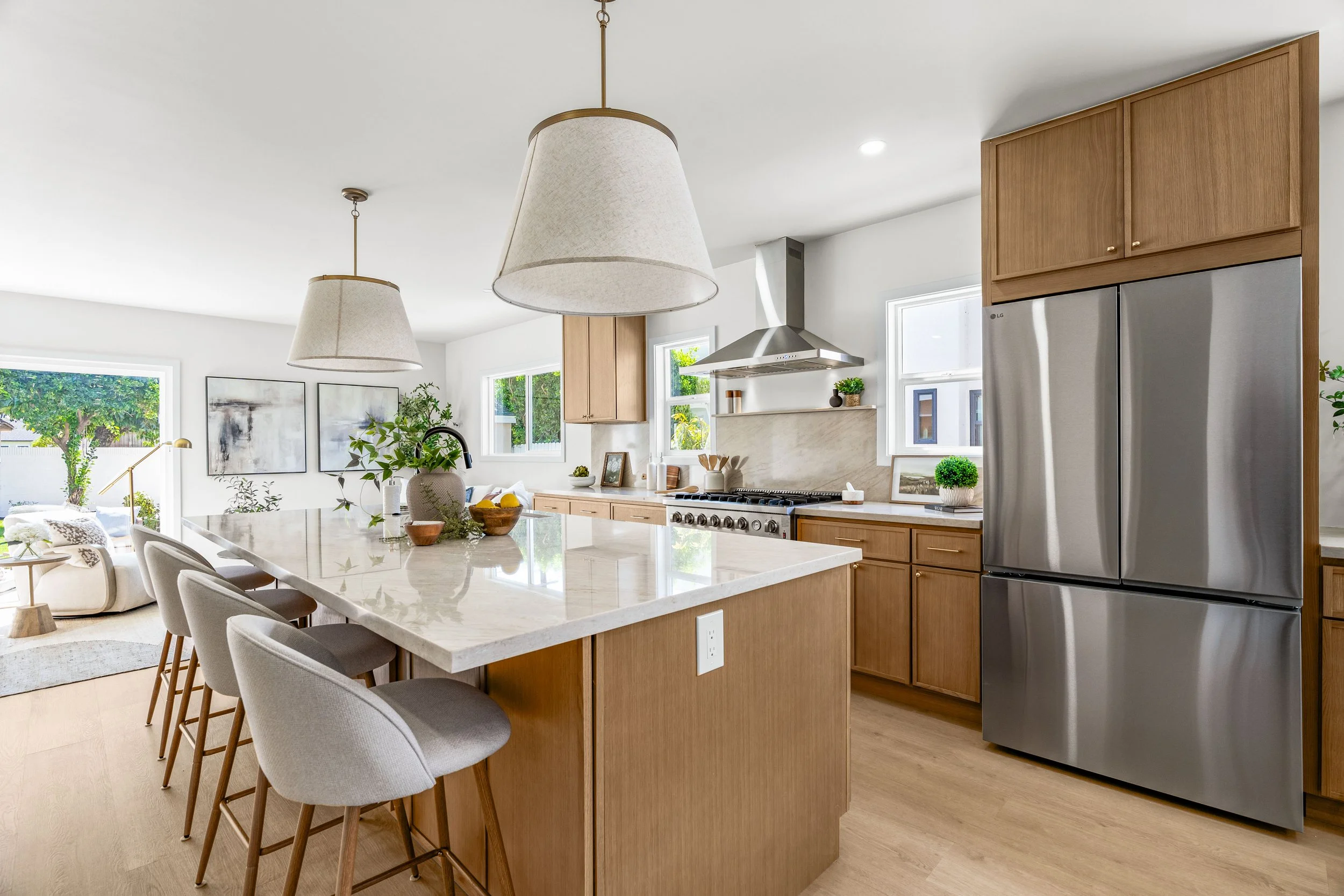 Modern kitchen with wood cabinets, stainless steel refrigerator, white marble island, and pendant lights.