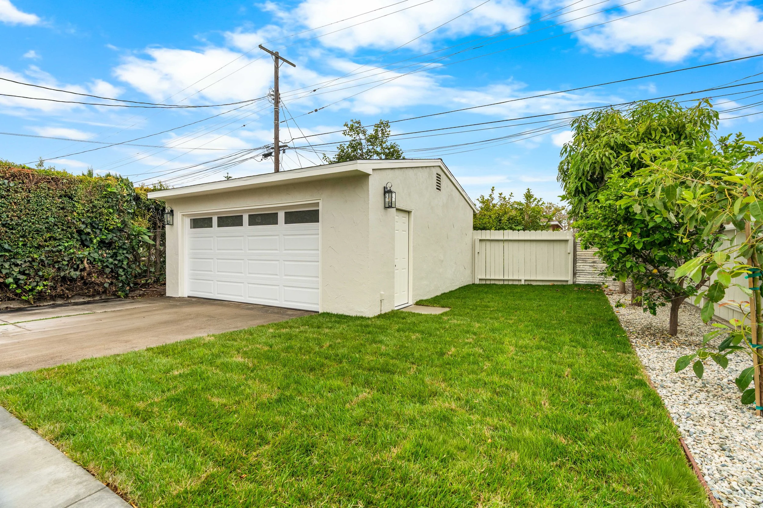 A suburban backyard with a white garage, green lawn, a tree, and a blue sky with some clouds.