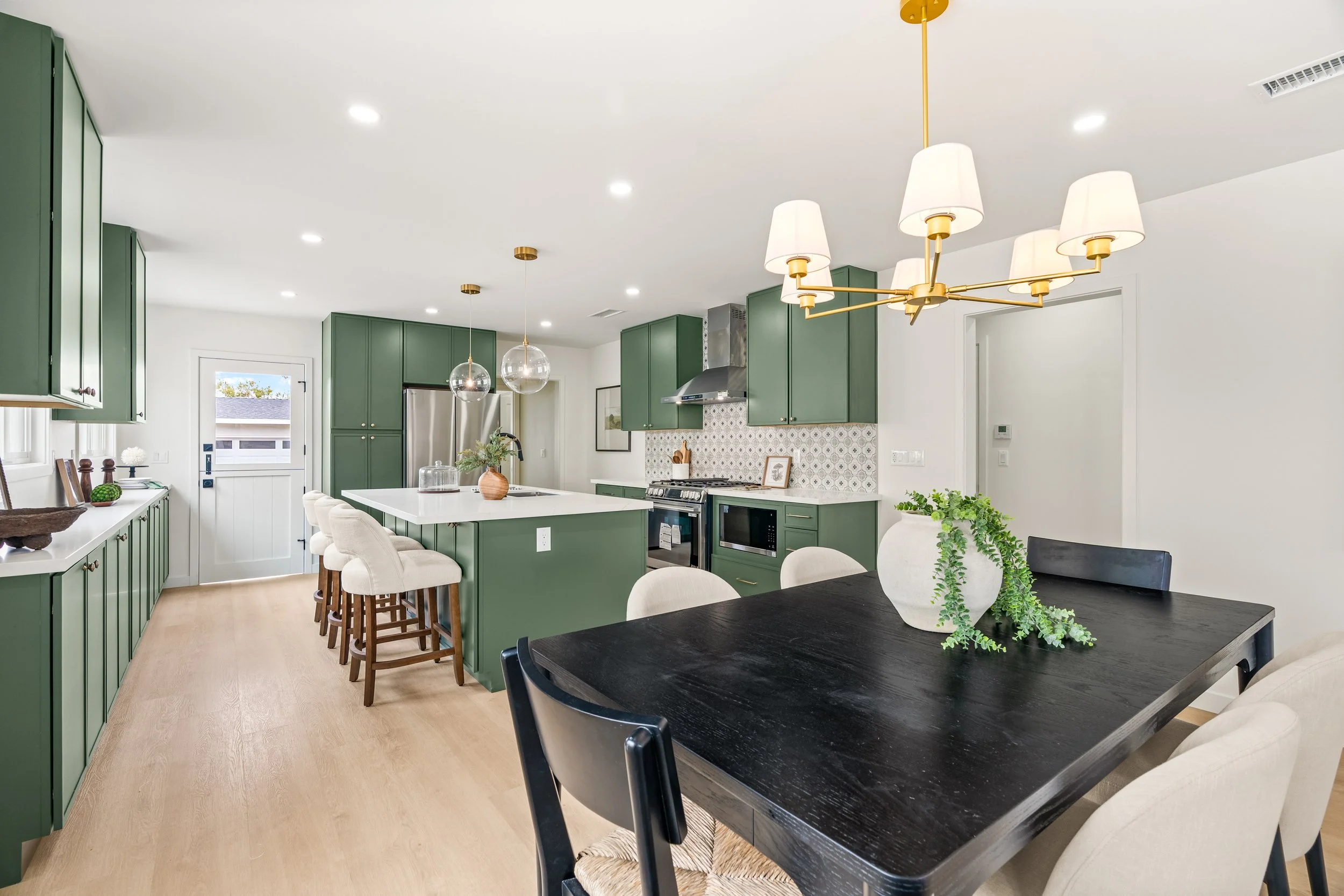 Modern kitchen with green cabinets, white countertops, a black dining table with white chairs, and pendant lights hanging from the ceiling.