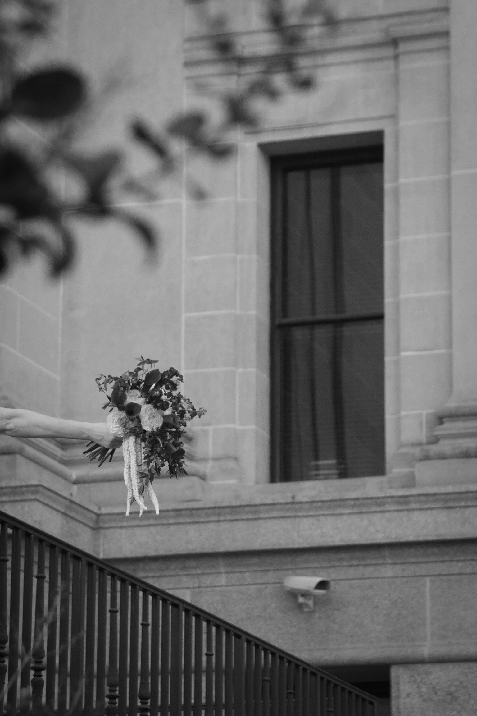 A floral arrangement hanging on a staircase bannister in front of a building with a large window and a stone exterior wall.